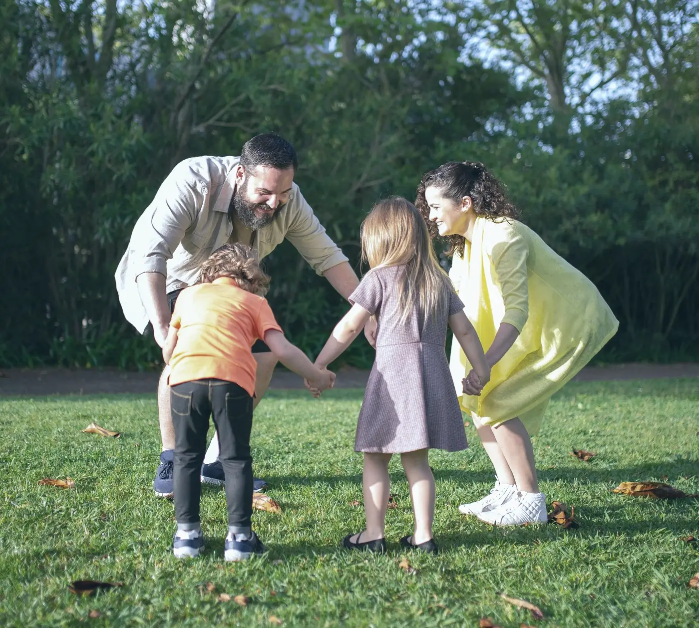 A family laughing together as they hold hands and play in a circle on the grass in a park
